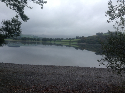 Grey sky, the green hills reflected in the still waters of the lake